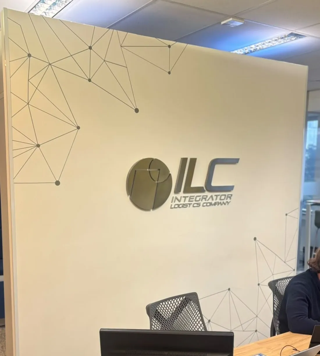 Parede do escritório da ILC com o grafismo de nós conectados e o logo em metal